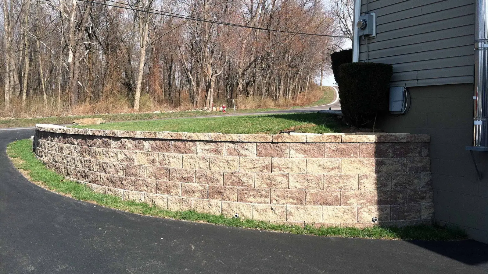 Split-face block retaining wall with weep holes along a curved asphalt driveway