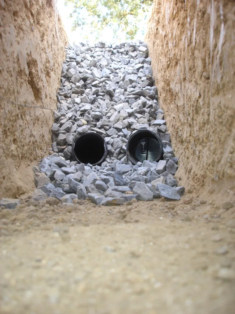 Drain trench lined with crushed rock holding two perforated drain pipes
