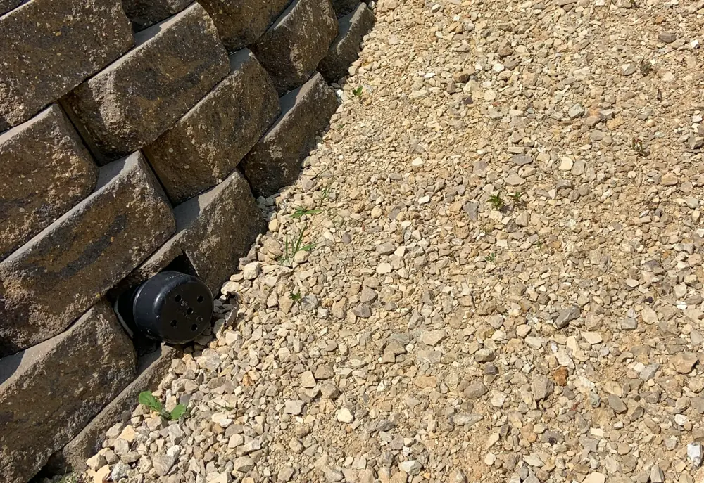 Drain pipe outlet at the base of a block retaining wall above a gravel bed